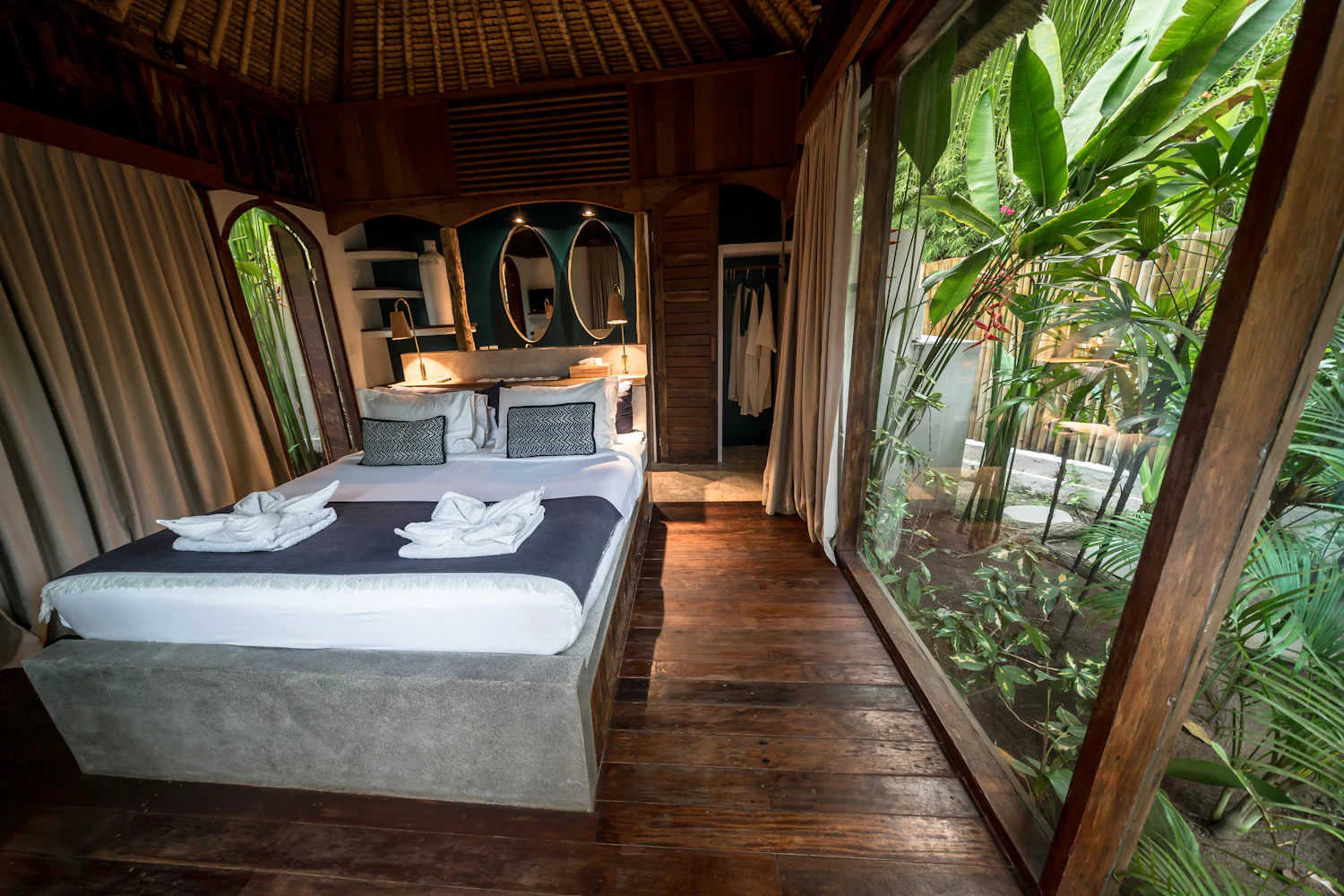 Bedroom with a timber floor and a glass wall opening onto a garden