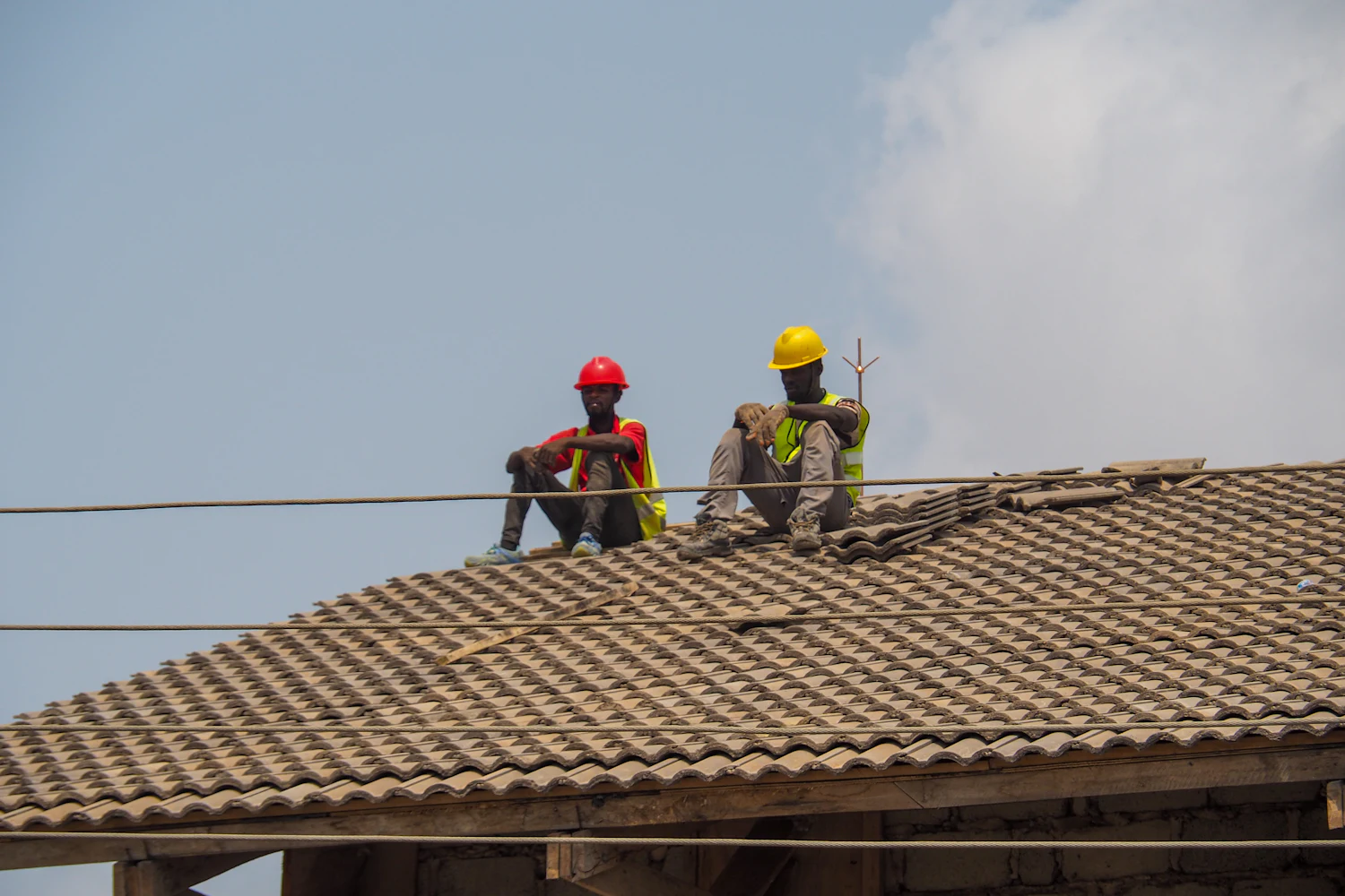 Two builders in hard hats sitting on a newly tiled roof